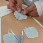 Hands applying electrotherapy pads on the back for muscle stimulation.